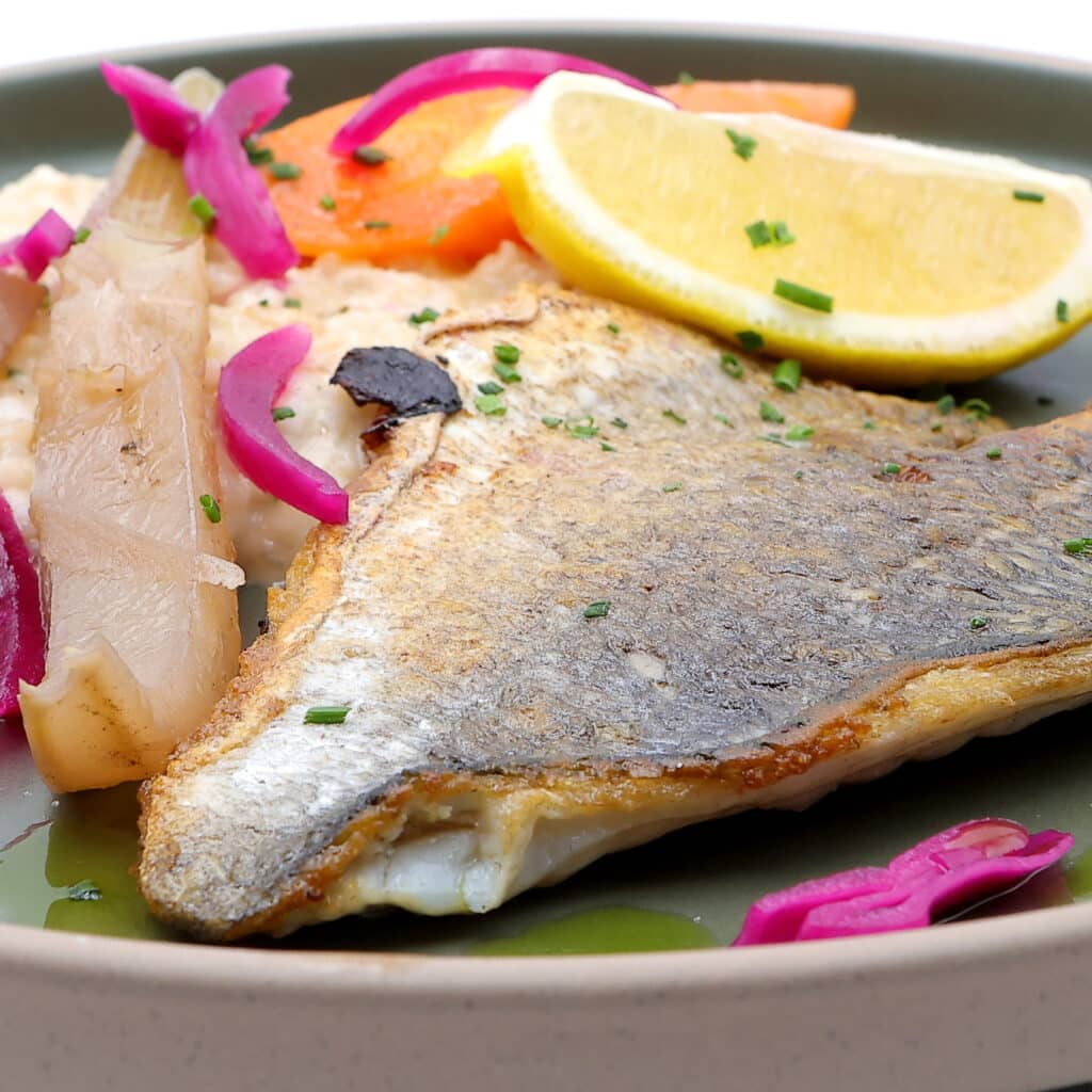 Dorade grillée à la peau croustillante, citron et risotto. Filet de dorade grillé peau croustillante sur risotto, garni de citron, carottes rôties, fenouil et oignons marinés roses vifs.